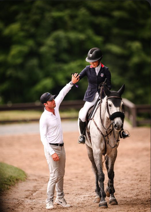 A trainer congratulating a rider on a gray horse in the ring